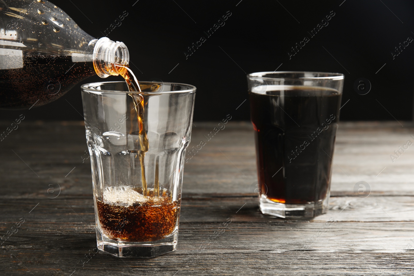 Photo of Pouring refreshing soda drink into glass on black wooden table against dark background