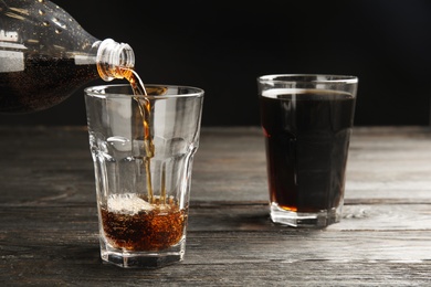 Pouring refreshing soda drink into glass on black wooden table against dark background