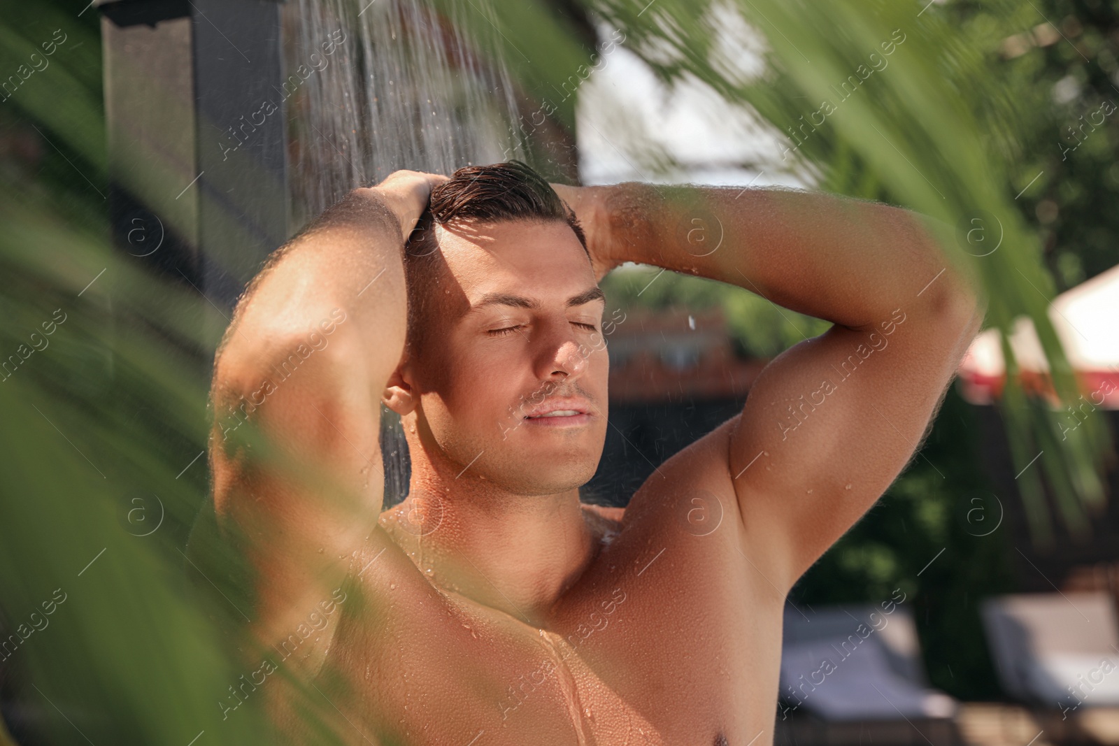 Photo of Man washing hair in outdoor shower on summer day