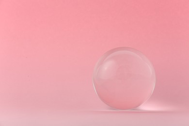 Photo of Transparent glass ball on light pink background. Space for text