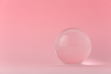 Transparent glass ball on light pink background. Space for text