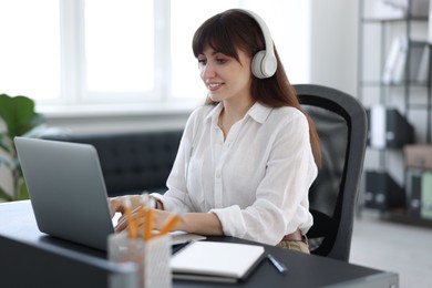 Woman in headphones watching webinar at table in office