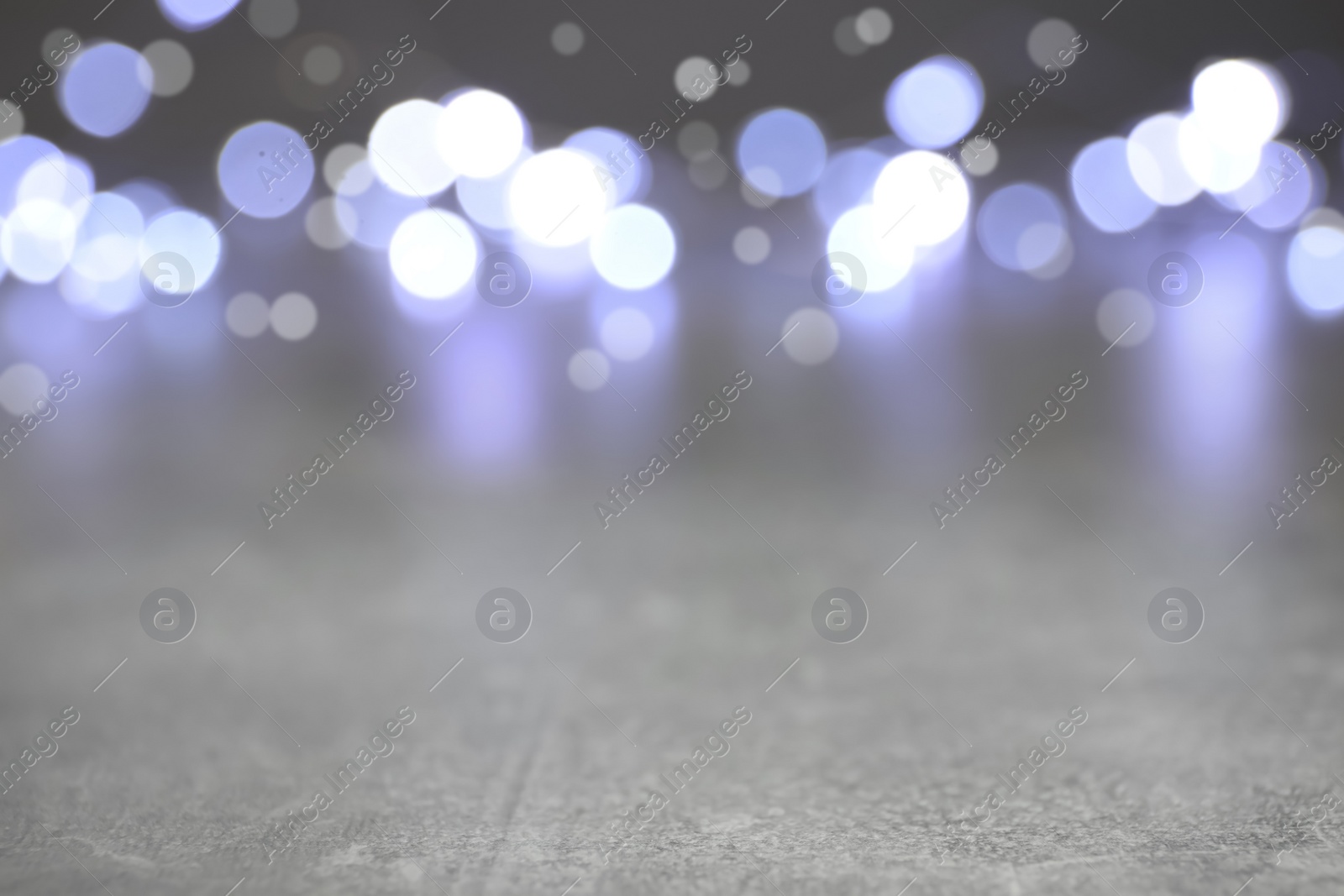 Photo of Blurred view of silver lights on grey table, space for text