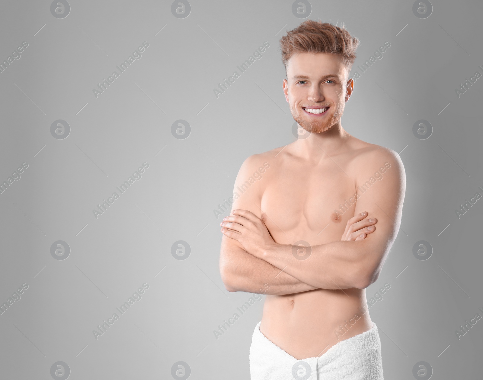 Photo of Portrait of young man with slim body in towel on grey background. Space for text