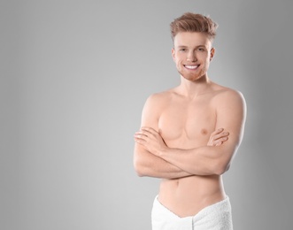 Portrait of young man with slim body in towel on grey background. Space for text