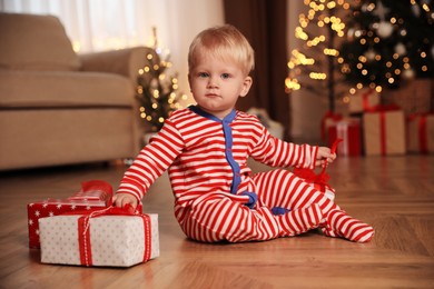 Baby in Christmas pajamas opening gift box indoors