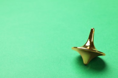 One golden spinning top on green background, closeup. Space for text