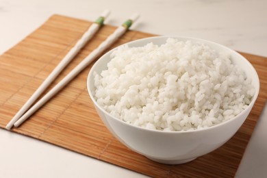 Bowl with delicious rice and chopsticks on white table