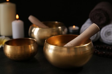 Photo of Golden singing bowls with mallets on black table against dark background