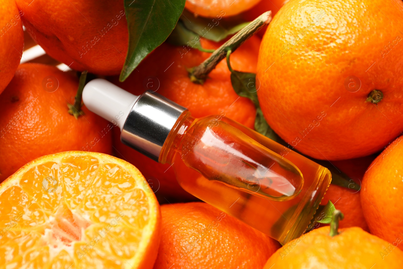 Photo of Bottle of tangerine essential oil with fresh fruits, closeup