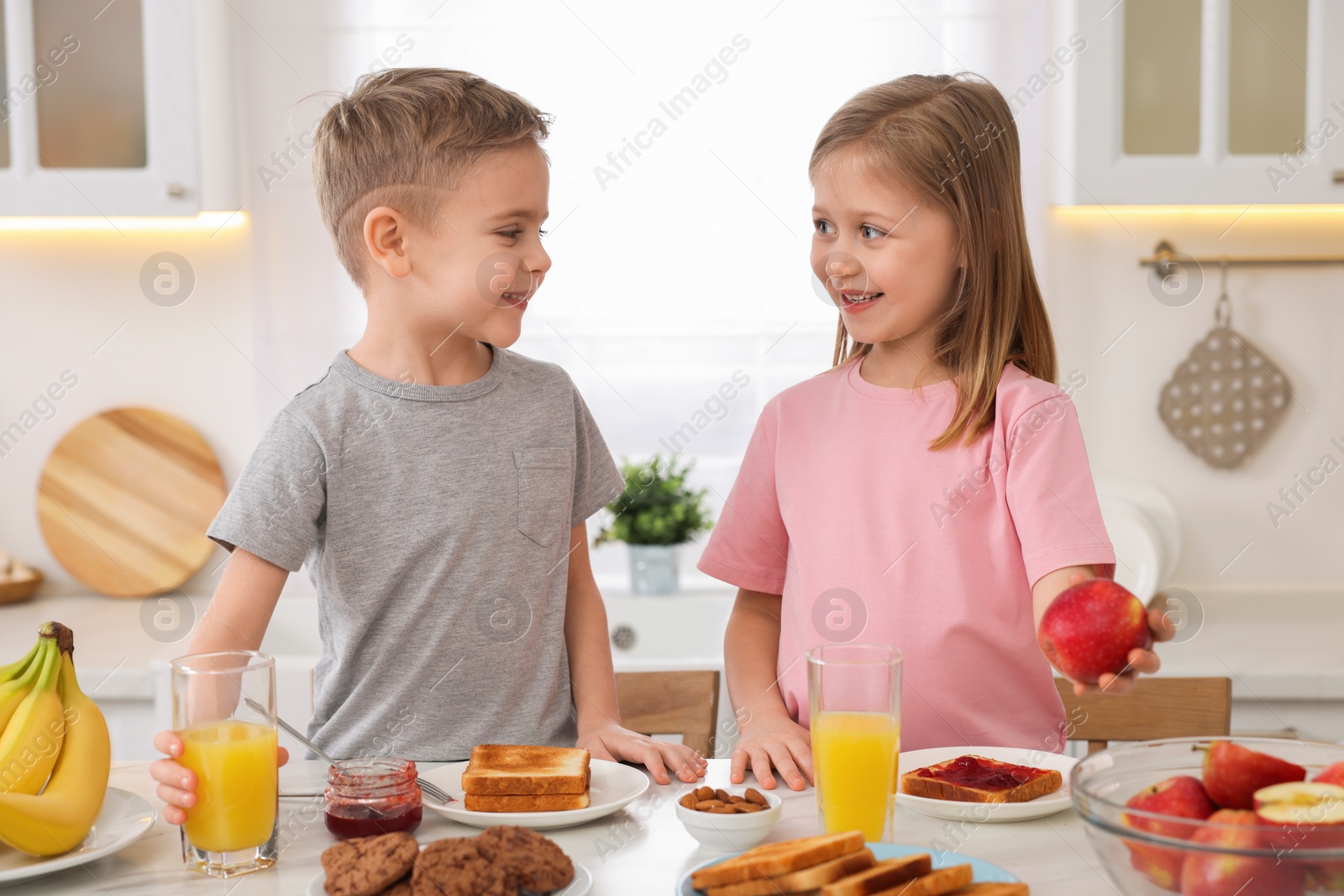 Photo of Little children having breakfast at table in kitchen