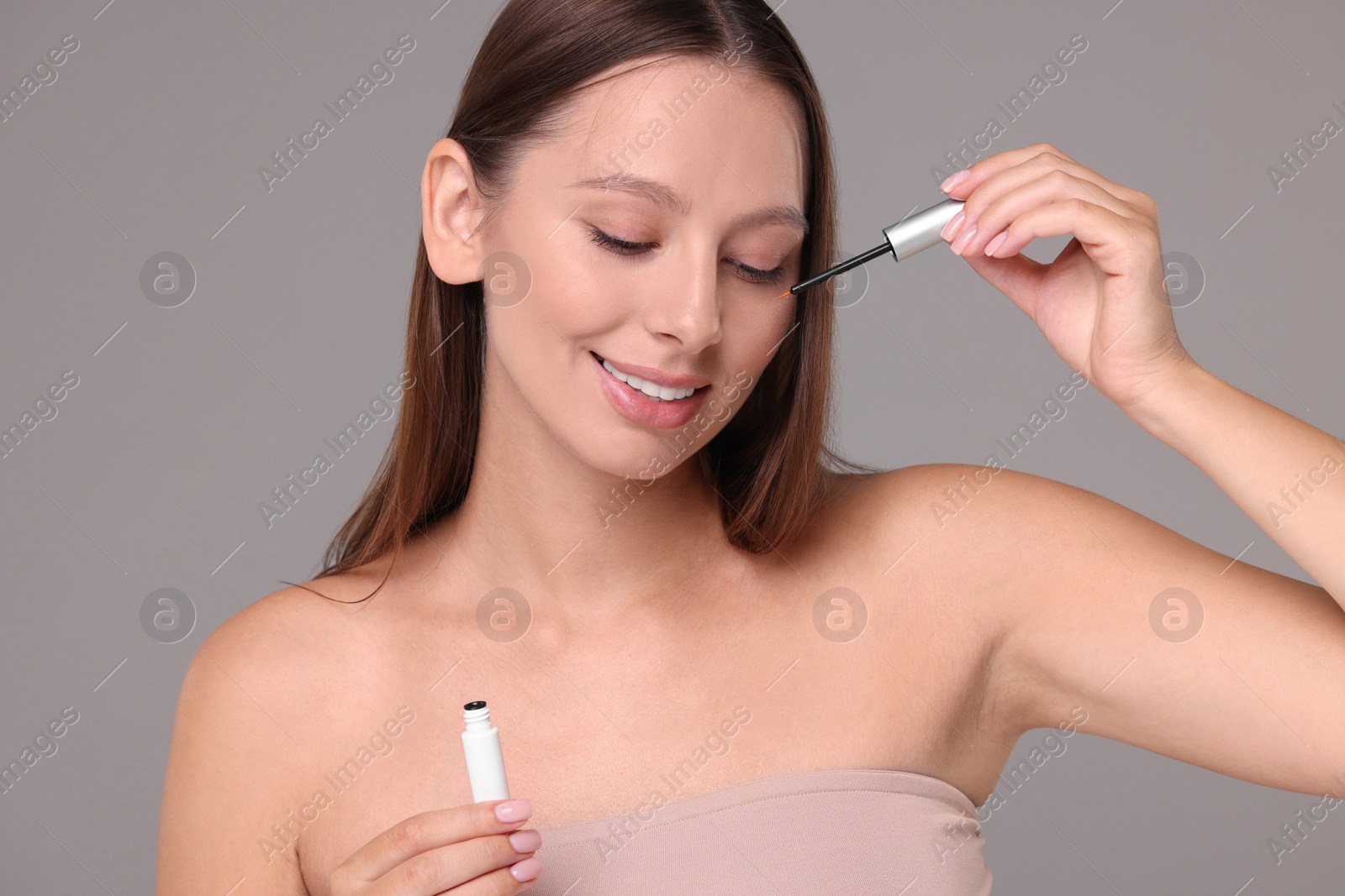 Photo of Beautiful woman applying serum onto eyelashes on grey background