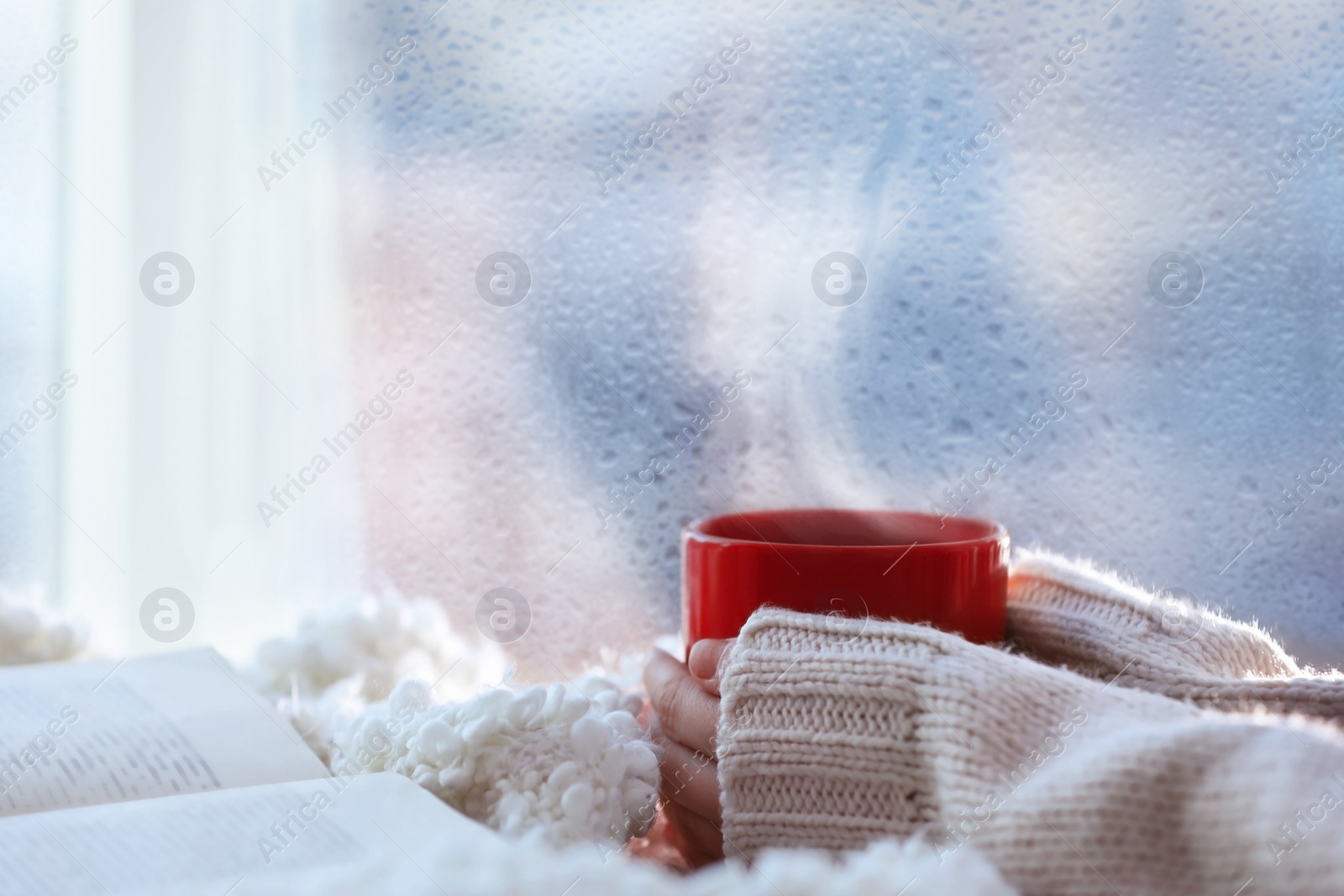 Image of Woman with cup of hot drink near window on rainy day, closeup