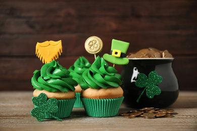Photo of Decorated cupcakes and pot with gold coins on wooden table. St. Patrick's Day celebration