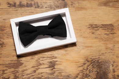 Stylish black bow tie in box on wooden table, top view. Space for text