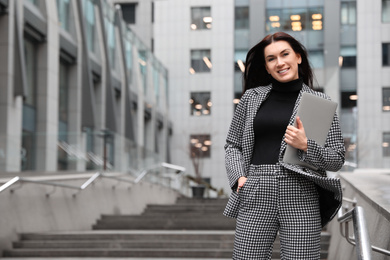 Beautiful woman in stylish suit with laptop outdoors. Space for text