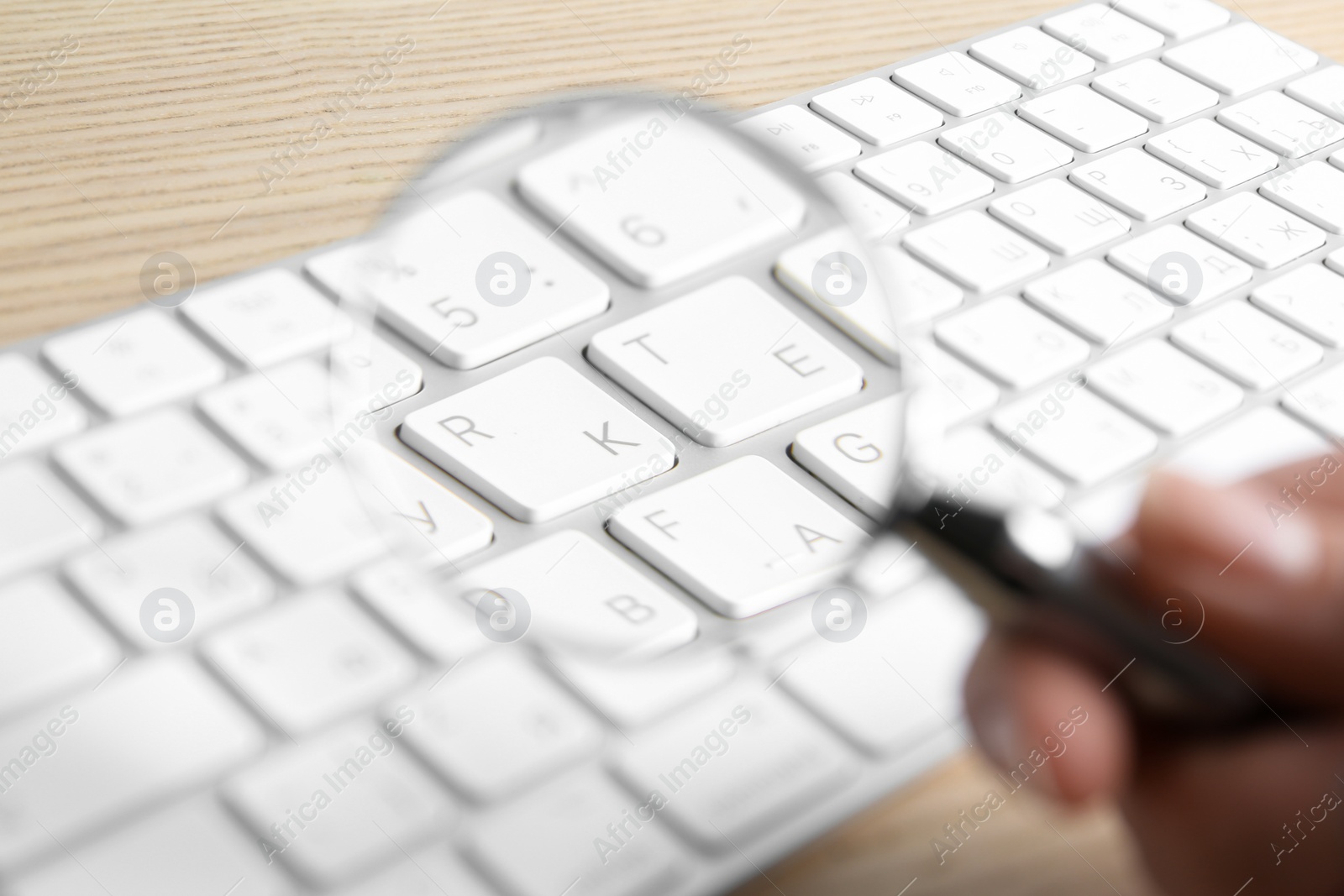 Photo of Woman looking through magnifying glass at computer keyboard on table, closeup. Search concept