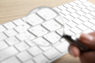 Woman looking through magnifying glass at computer keyboard on table, closeup. Search concept