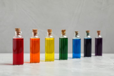 Photo of Glass bottles with different food coloring on light grey marble table