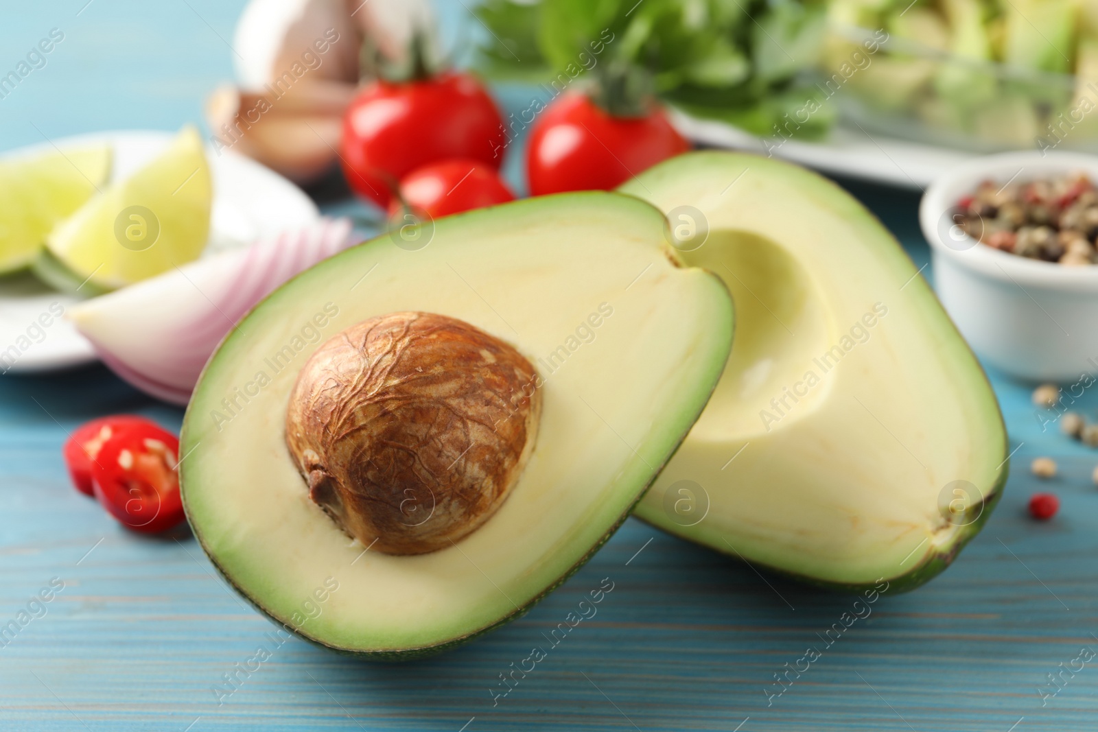 Photo of Fresh ripe avocado and other ingredients for guacamole on light blue wooden table, closeup