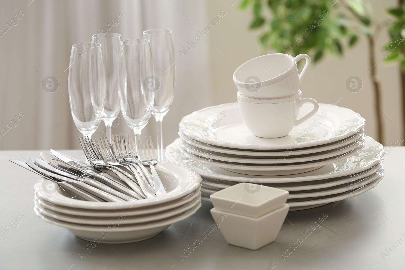 Photo of Set of clean dishware, cutlery and champagne glasses on table indoors