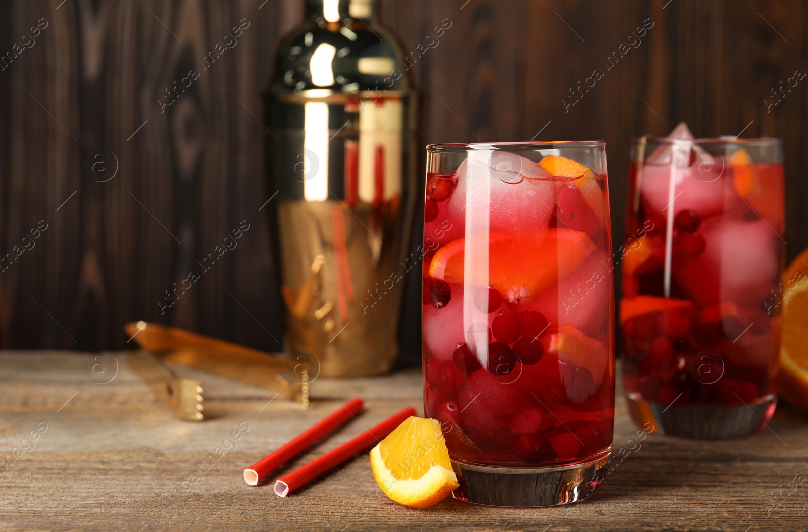 Photo of Tasty cranberry cocktail with ice cubes and orange in glasses on wooden table, space for text