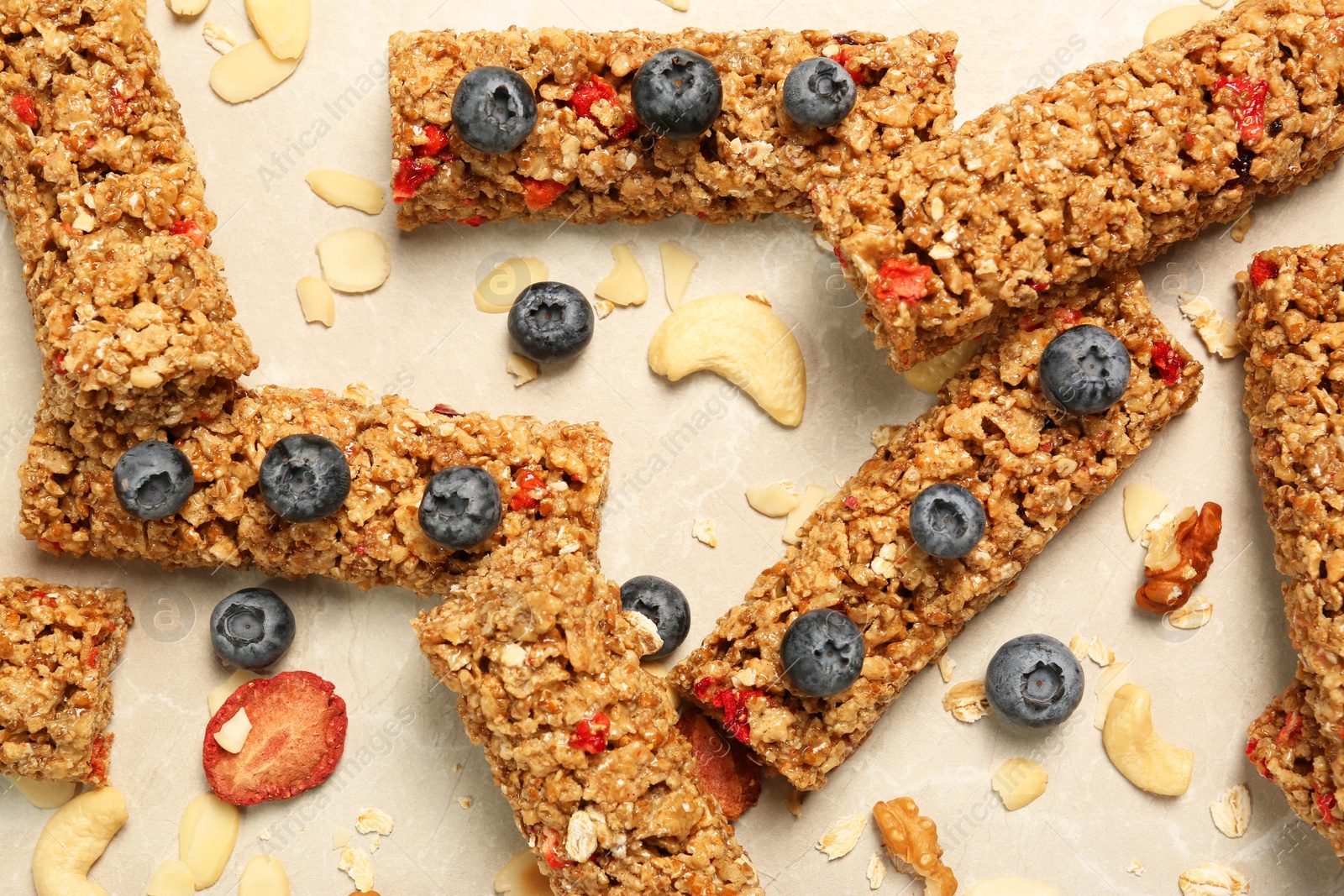 Photo of Tasty granola bars, blueberries and nuts on beige marble table, flat lay