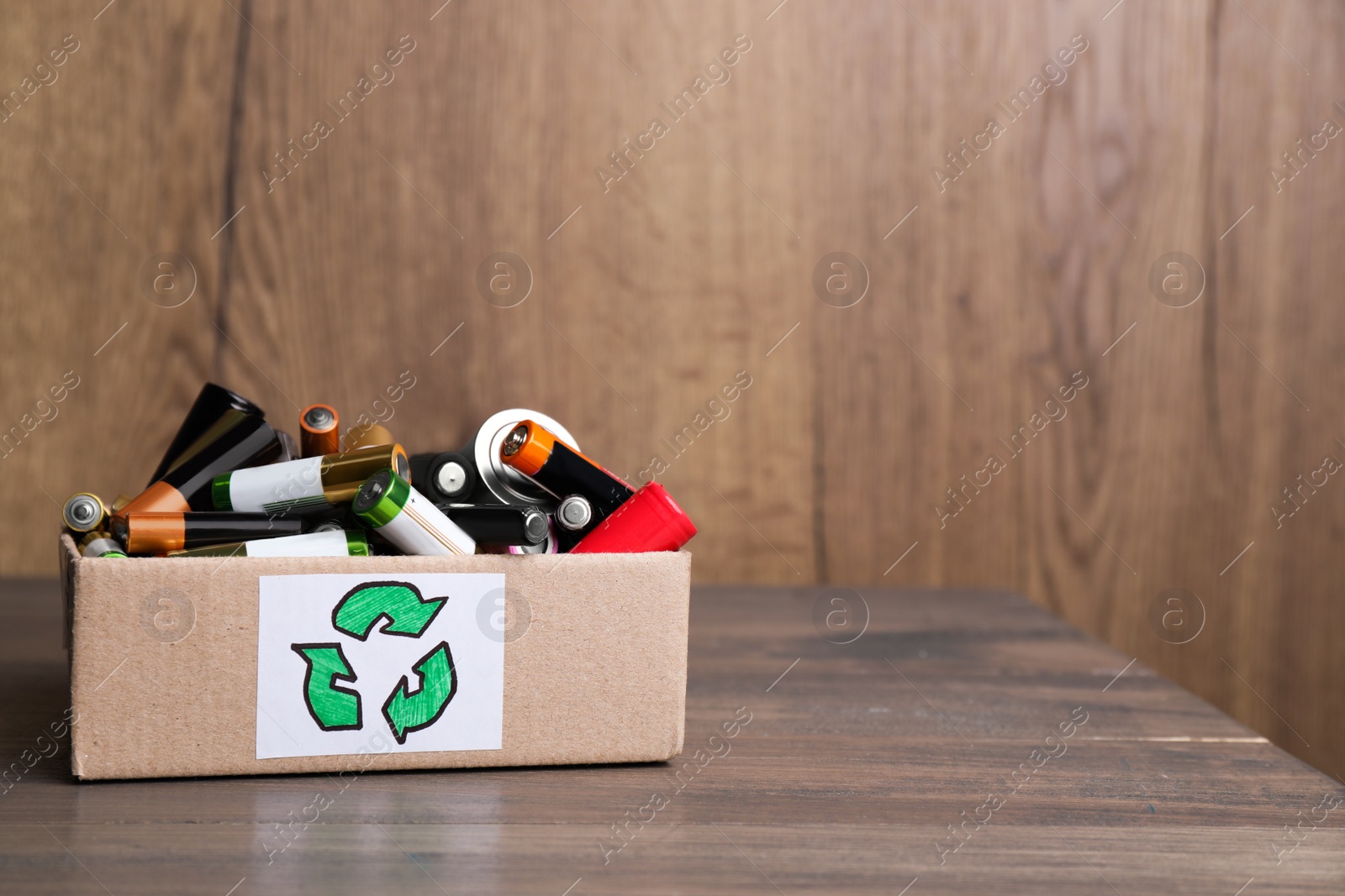 Image of Used electric batteries in cardboard box with recycling symbol on wooden table. Space for text