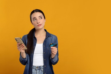 Photo of Confused woman with credit card and smartphone on orange background, space for text. Debt problem