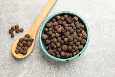 Photo of Aromatic allspice pepper grains in bowl and spoon on grey table, top view