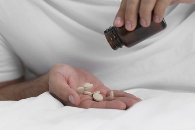 Photo of Man pouring antidepressants from bottle on bed, closeup