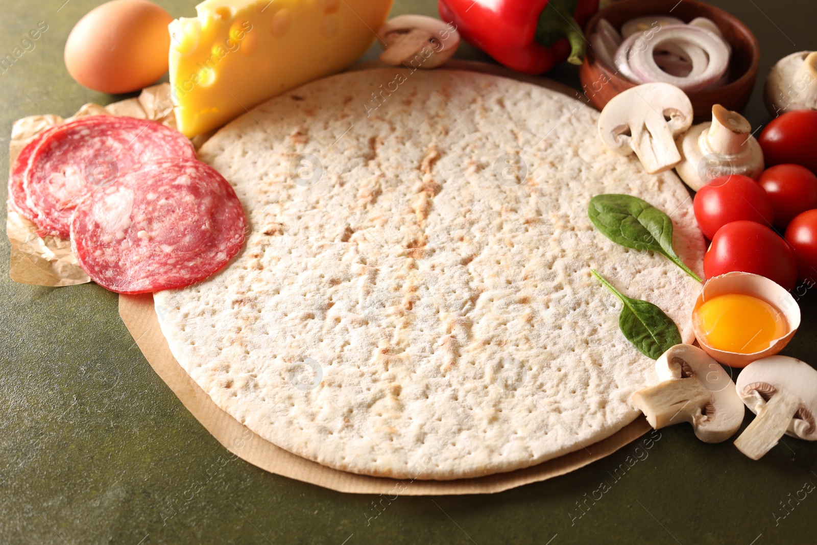 Photo of Pizza base and products on green textured table, closeup