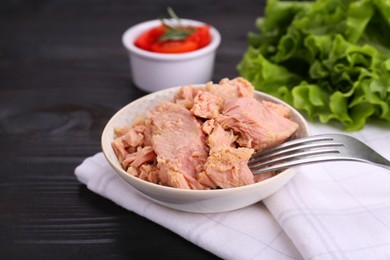 Bowl with canned tuna with fork on black wooden table, closeup