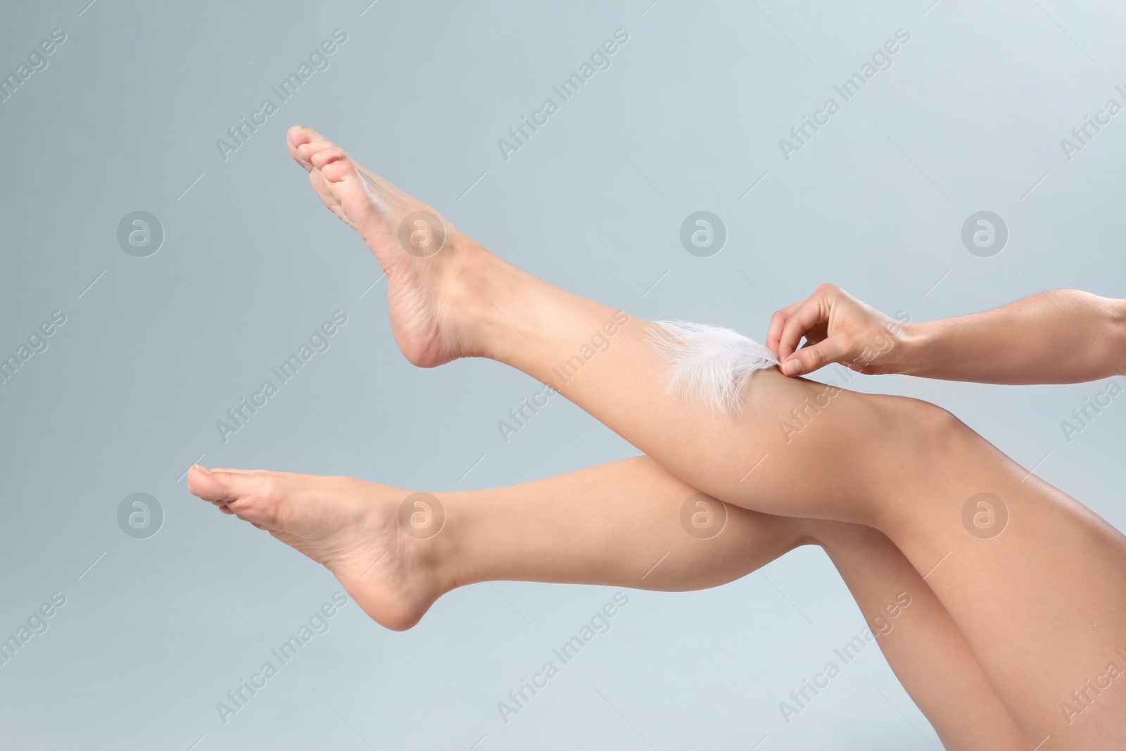 Photo of Woman touching leg with feather on grey background, closeup. Epilation procedure