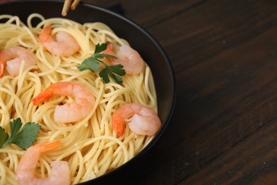 Photo of Tasty spaghetti with shrimps and parsley in bowl on wooden table, closeup. Space for text