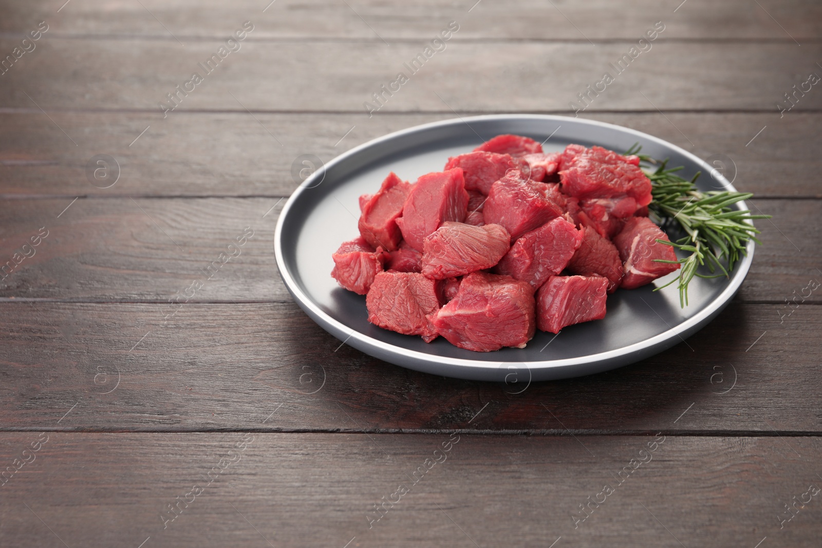 Photo of Pieces of raw beef meat with rosemary on wooden table. Space for text