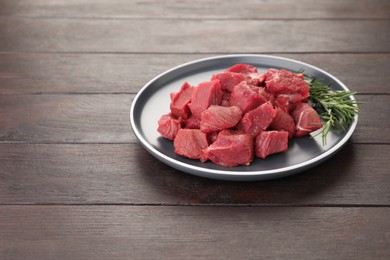 Pieces of raw beef meat with rosemary on wooden table. Space for text