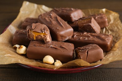Many tasty chocolate bars with caramel and nuts on wooden table, closeup