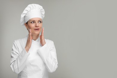 Photo of Surprised woman chef in uniform on grey background, space for text