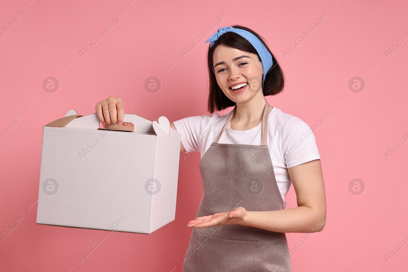 Photo of Happy confectioner with cake box on pink background