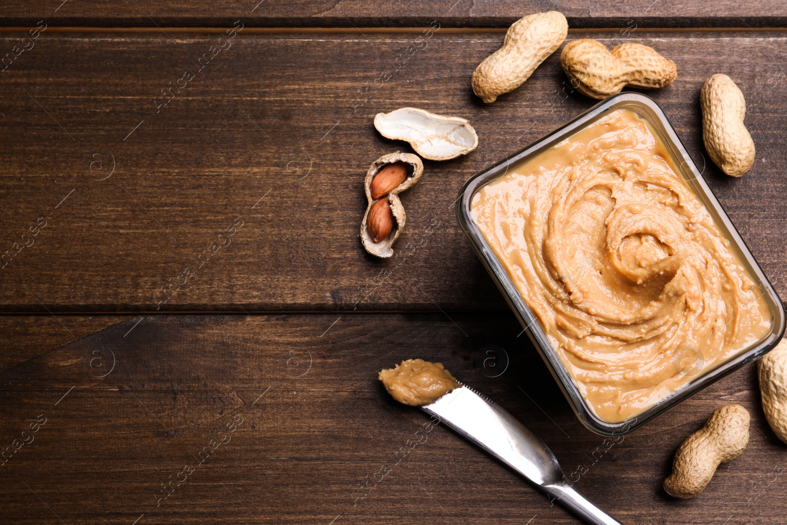 Photo of Yummy peanut butter in glass bowl on wooden table, flat lay. Space for text