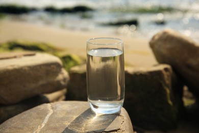 Glass of fresh water on stone near sea