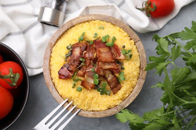 Photo of Cooked cornmeal with bacon and microgreens in bowl on light grey table, flat lay