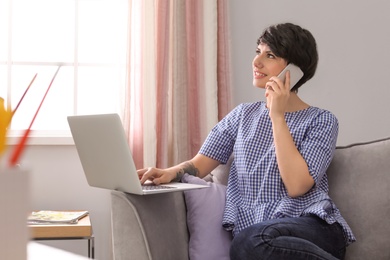Photo of Young woman talking on mobile phone while working with laptop at home