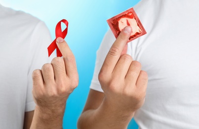 Men with condom and AIDS awareness ribbon on light blue background, closeup