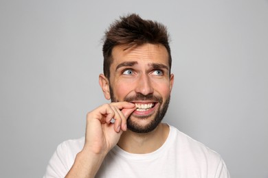 Man biting his nails on grey background