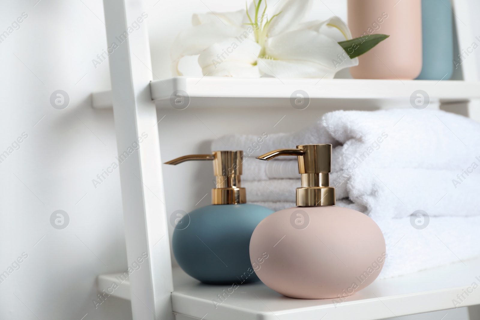 Photo of Stylish soap dispensers and towels on shelf near light wall