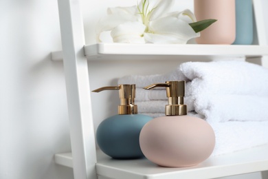 Photo of Stylish soap dispensers and towels on shelf near light wall