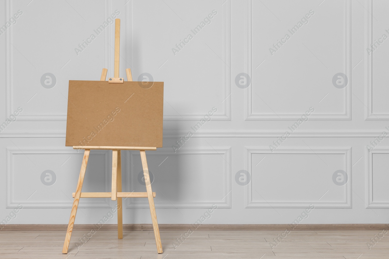 Photo of Wooden easel with blank board near white wall indoors. Space for text