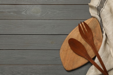 Wooden board, spoon and fork near towel on table, flat lay with space for text. Cooking utensils